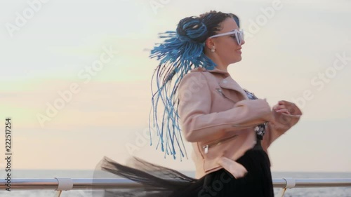 Portrait of beautiful girl with african kanekalon blue braids and heart shaped sunglasses dancing on sea background. Afro hairstyle, freaky dyed hair. Hipster having fun. photo