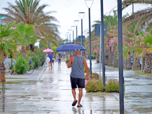 un uomo con omrello passeggia su un lungomare mentre piove