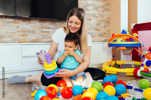 Young and happy mother playing in house with her little son