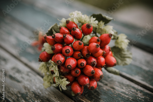 Beautiful autumn bouquet of red hips and green hops on the old textured wooden table with blurred background
