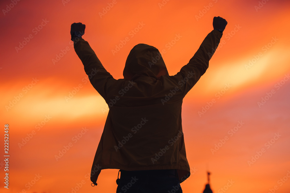 Silhouette of successful man with raised hands in hood at sunset, back view
