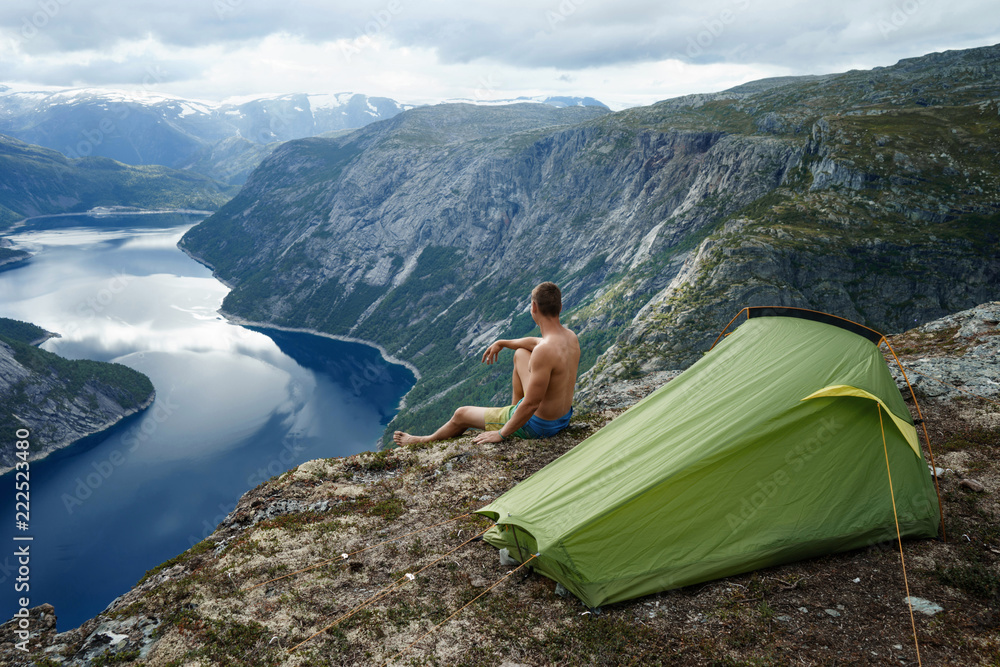 Fototapeta premium Norwegian fjord landscape with camping tent and young traveller. concept of travel and freedom