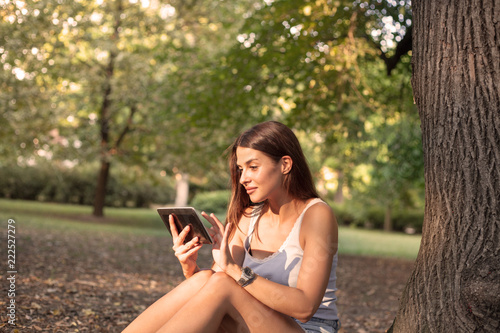 Woman reading tablet and enjoy rest in a park under tree .