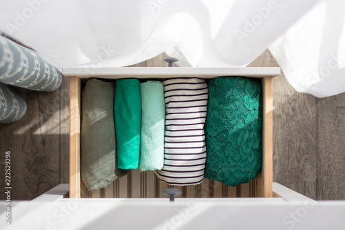 Fotografie The clothes of green tones are neatly folded in the chest of drawers near the wi