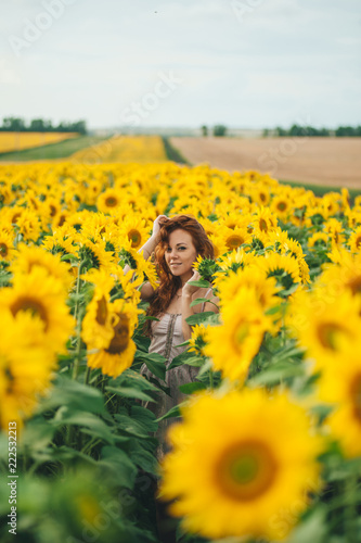 Young beautiful woman in a dress among blooming sunflowers. Agroculture.