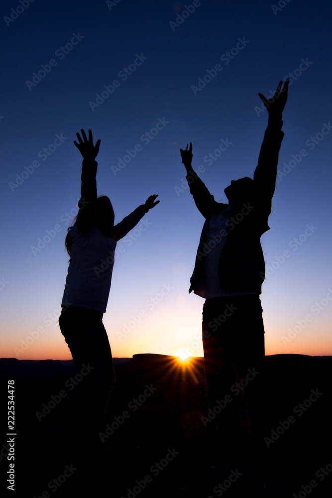 silhouette of a man and woman with outstretched arms raised