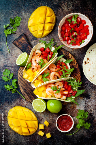 Mexican shrimp tacos with avocado, tomato, mango salsa on rustic stone table. Recipe for Cinco de Mayo party. Top view, overhead, flat lay.