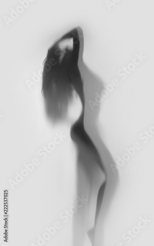 Beautiful and sexy woman body silhouette in attractive pose behind a diffuse curtain.