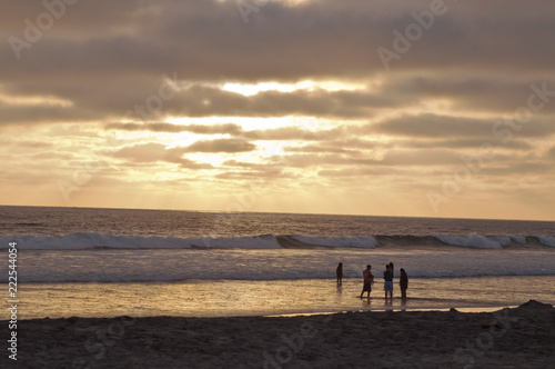 Four people in the surf of the Pacific ocean in southern California, USA under a golden sunset in summer