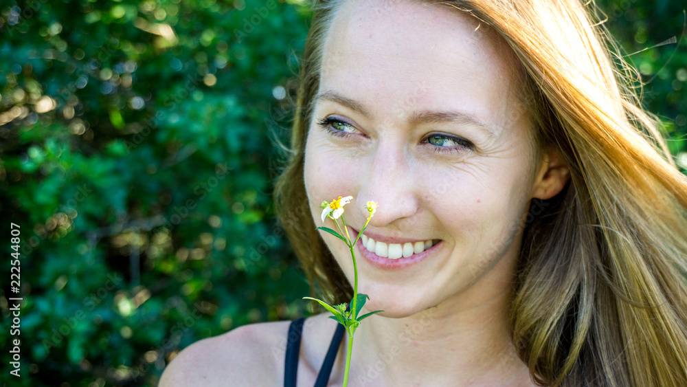 Cute close portrait of young blonde woman face smiling with blue clear eyes and daisy flower isolated looking left