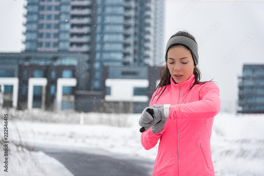 Winter running smartwatch fitness girl in cold snow weather jogging outside  on street wearing smart watch and windproof clothes with gloves, headband,  pink jacket in city background. Stock-Foto | Adobe Stock