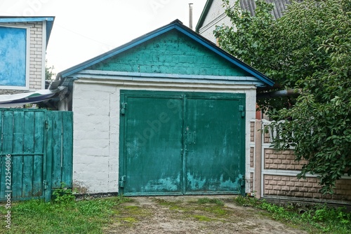 one gray brick garage with closed glazed green gates on the street in the grass
