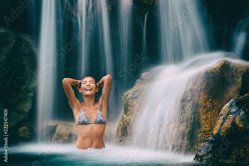 Waterfall woman smiling happy in natural pool. Bikini girl having fun in hawaiian travel destination waterfalls in natural pool. Sexy beautiful girl in pristine nature enjoying summer travel vacation.