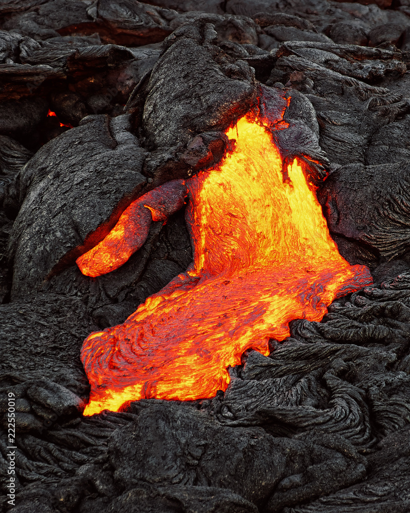 A lava flow emerges from a rock column and pours into a black volcanic