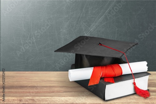 Graduation mortarboard on book on background