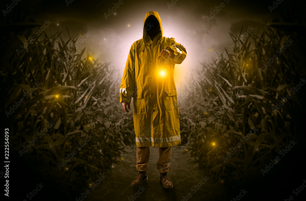 Naklejka premium Man in raincoat at night coming from thicket and looking something with glowing lantern 