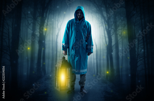 Man in raincoat coming from dark forest with glowing lantern in his hand concept   © ra2 studio