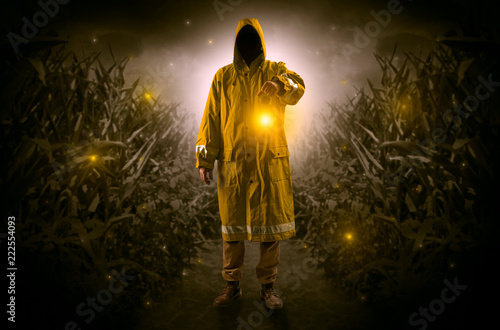 Man in raincoat at night coming from thicket and looking something with glowing lantern  