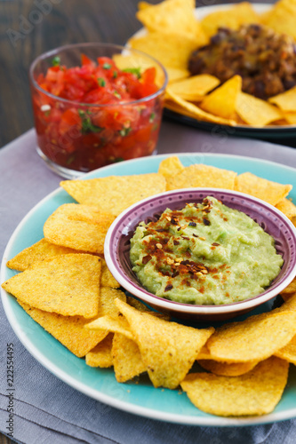 Mexican food: chili con carne, guacamole and salsa served with nachos. Dark table, high resolution.
