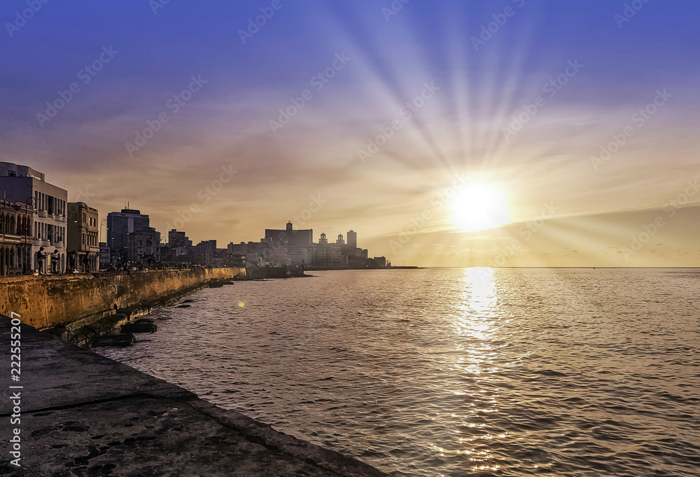 Sunset over Malecon and Atlantic Ocean with residential building and visible sun rays - Havana, Cuba 