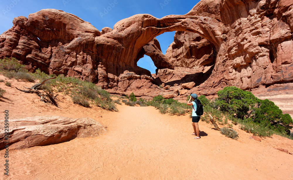 Woman photographing double arch during summertime in Utah