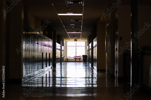 Straight view of darkly lit hallway with bright light at end and lockers covering the walls on either side 