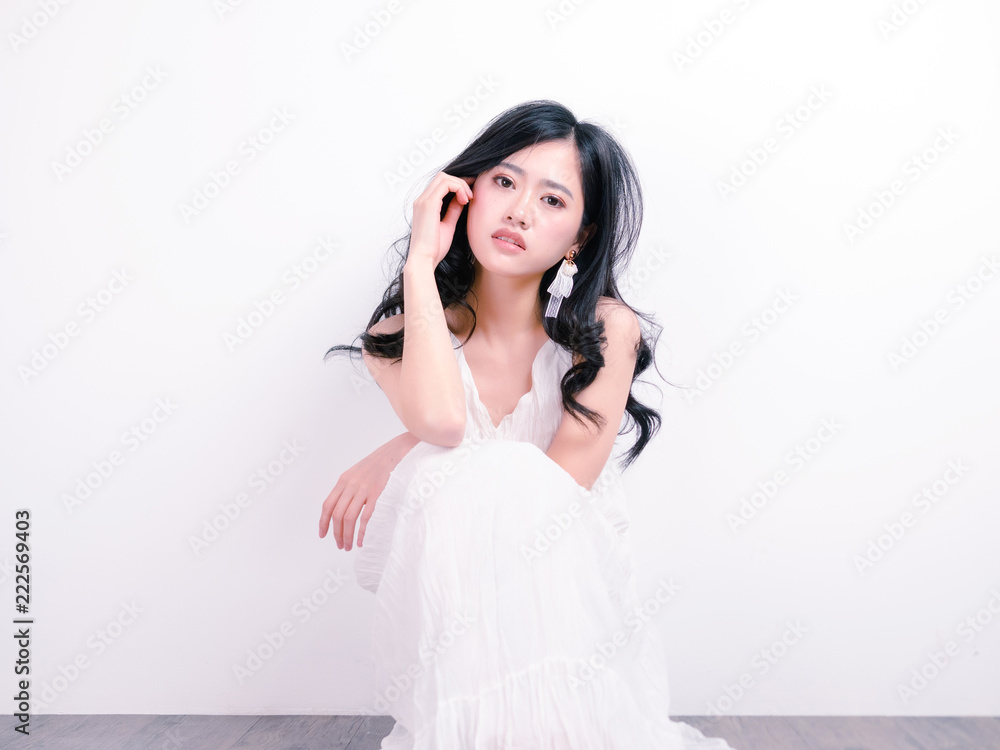 Beautiful Chinese girl sit on floor with hand on face against white wall background, portrait of romantic young female looking at camera with sexy expression. Beautiful Chinese girl sit on floor with hand on face against white wall background, portrait of romantic young female looking at camera with sexy expression.