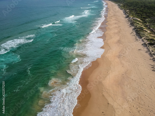 Aerial view of an ocean beach with waves, sand and bush