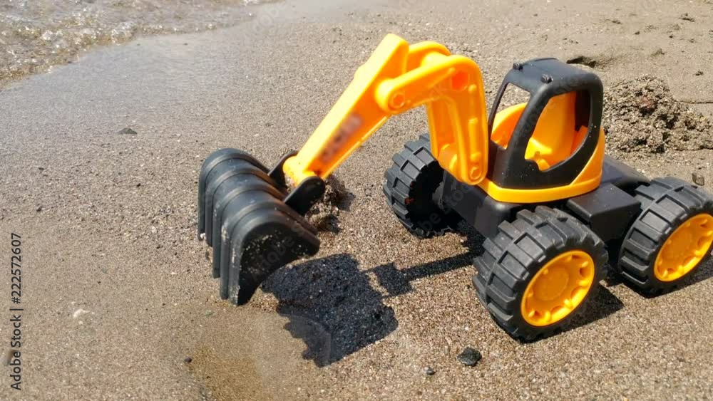 Closeup 4k video of toy orange excavator standing on sand sea beach Closeup 4k video of toy orange excavator standing on sand sea beach