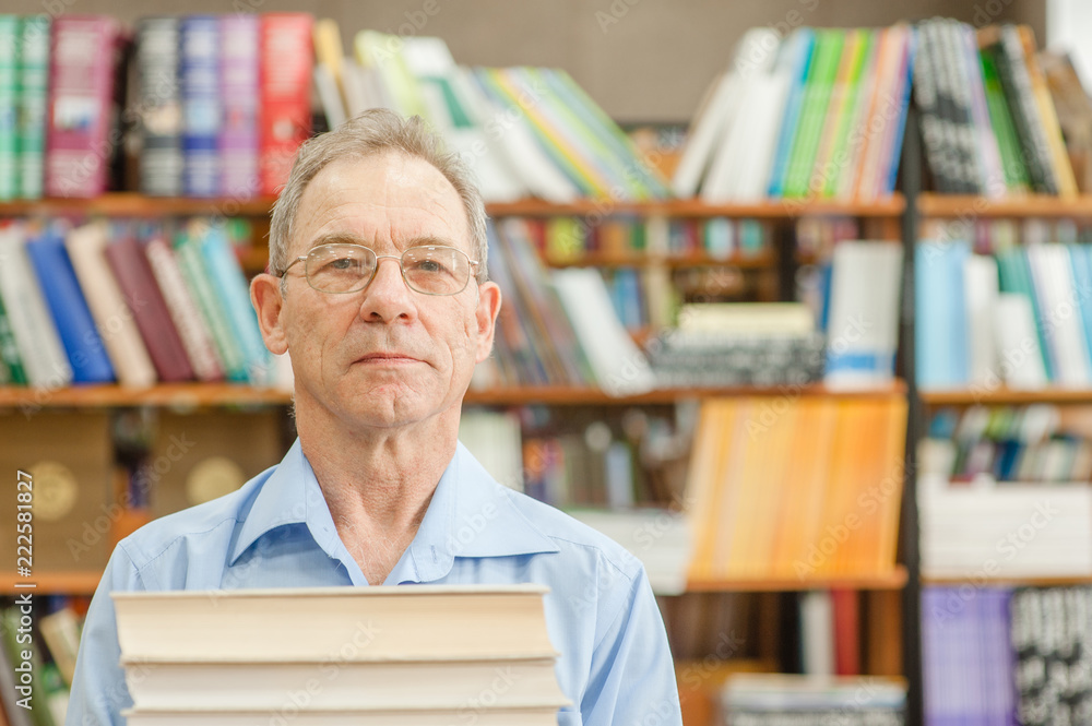 Senior man holds a pile of books in the library. Space for text Senior man holds a pile of books in the library. Space for text