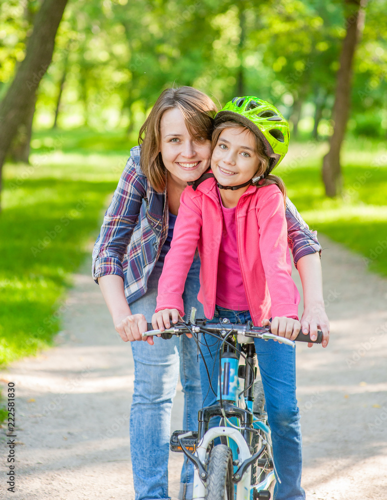 Smiling mom teaches her daughter to ride a bicycle in the park Smiling mom teaches her daughter to ride a bicycle in the park