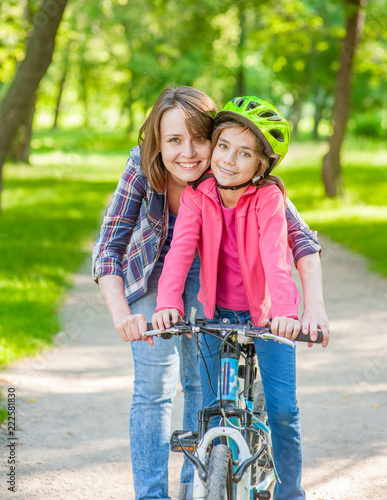 Smiling mom teaches her daughter to ride a bicycle in the park © Ermolaev Alexandr