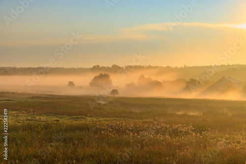 Fog over village houses in orange rays of rising sun in autumn morning. Nature landscape