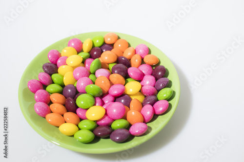 Many colored candies on a green plate isolated in a white background