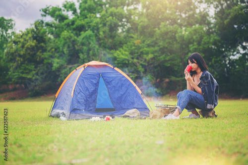 Asian pretty girl enjoy with hot drink beside the tent. Camping trip in nature.