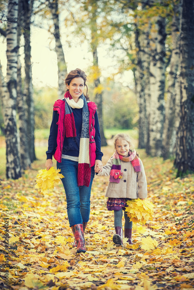 Smiling little girl and her mother enjoy walk in autumn park and play with bright autumn leaves Smiling little girl and her mother enjoy walk in autumn park and play with bright autumn leaves