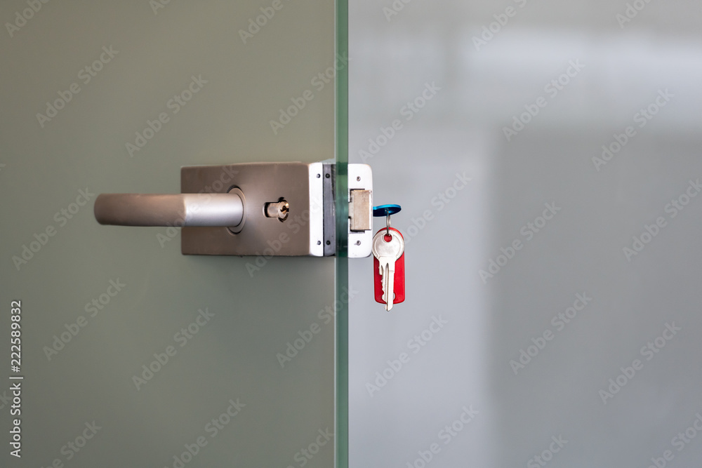Modern glass door with metal alloy handles and key chain in lock, home or office security concept Modern glass door with metal alloy handles and key chain in lock, home or office security concept