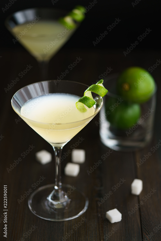 Two daiquiris served in cocktail glasses, garnished with lime zest. Dark wooden background, high resolution.