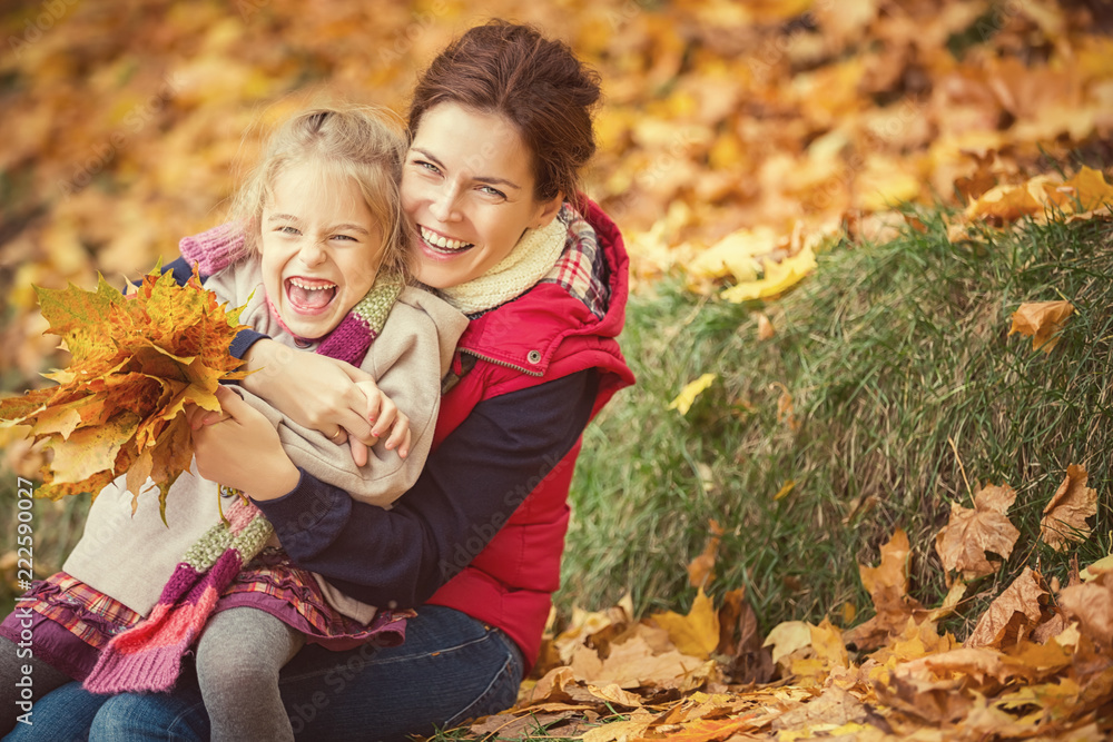 Happy little girl and her mother enjoy walk in autumn park and play with bright autumn leaves Happy little girl and her mother enjoy walk in autumn park and play with bright autumn leaves