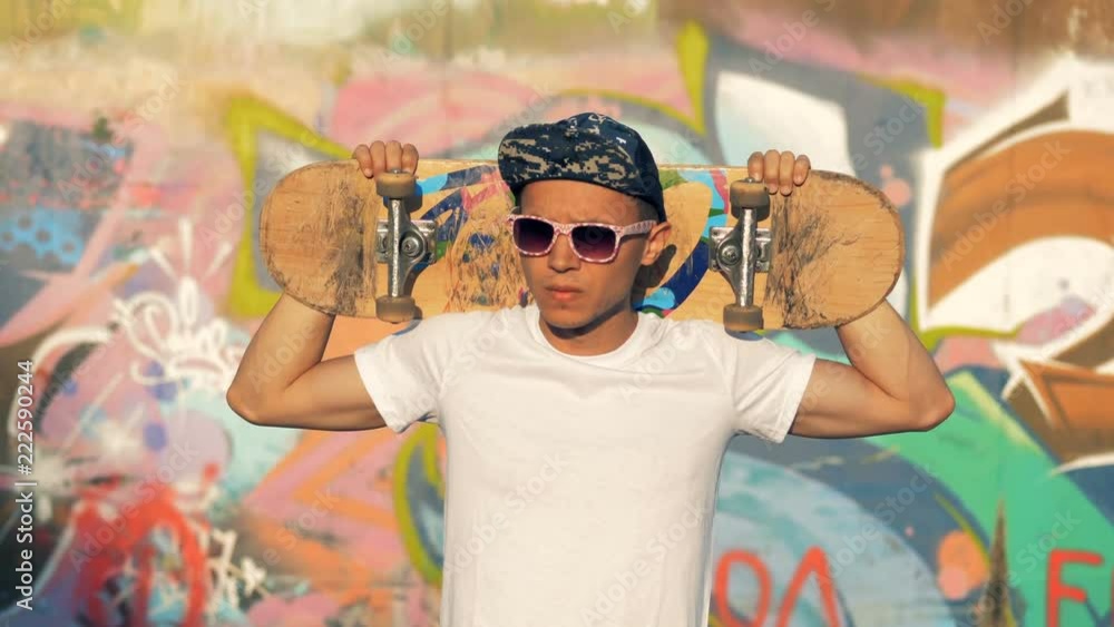 Young teenager skater portrait. Person with a skateboard stands near a wall on a street. Young teenager skater portrait. Person with a skateboard stands near a wall on a street.