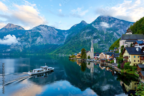 Scenic picture-postcard view of famous Hallstatt mountain village with Hallstatter lake and boat in Austrian Alps. Autumn sunset on Hallstatt lake with beautiful clouds.