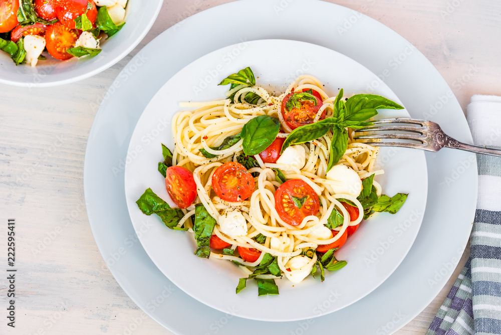 Italian food - Spaghetti caprese in a plate on a light rustic background, top view. Pasta with mozzarella, cherry tomatoes and basil