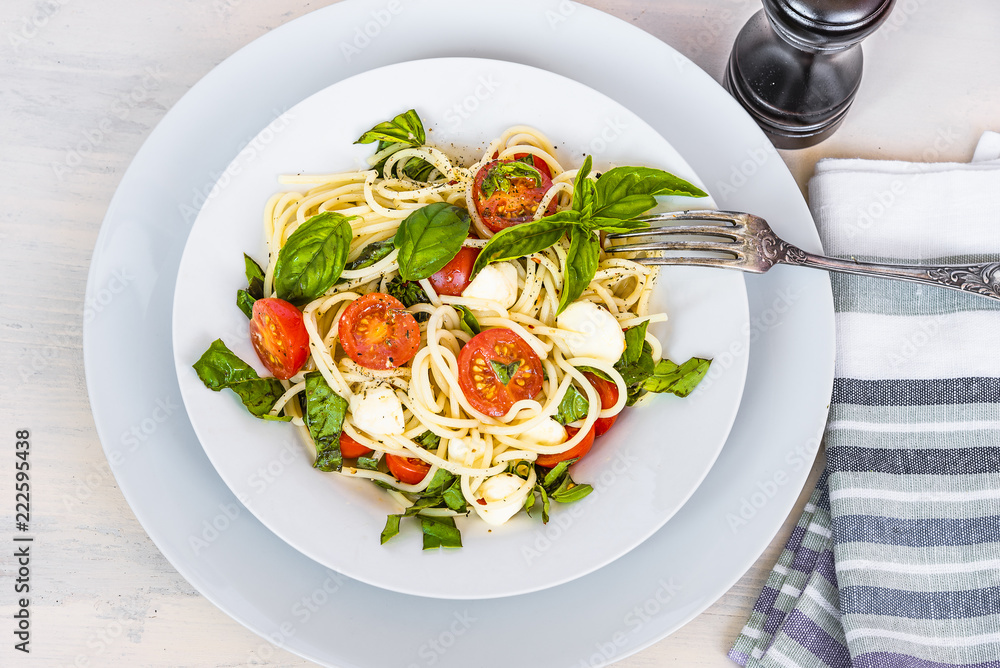Italian food - Spaghetti caprese in a plate on a light rustic background, top view. Pasta with mozzarella, cherry tomatoes and basil Italian food - Spaghetti caprese in a plate on a light rustic background, top view. Pasta with mozzarella, cherry tomatoes and basil