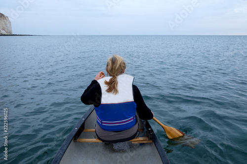 srear view of sixty year old woman kayaking in the sea she has long hair and a life jacket on in the distance are white cliffs
