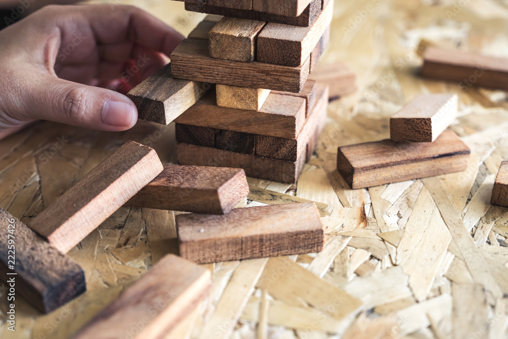 Closeup image of a hand holding and playing Jenga or Tumble tower wooden block game Closeup image of a hand holding and playing Jenga or Tumble tower wooden block game