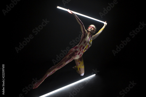 Mujer joven haciendo danza contemporánea con tubos de luces con el cuerpo pintado en un estudio de fotografía