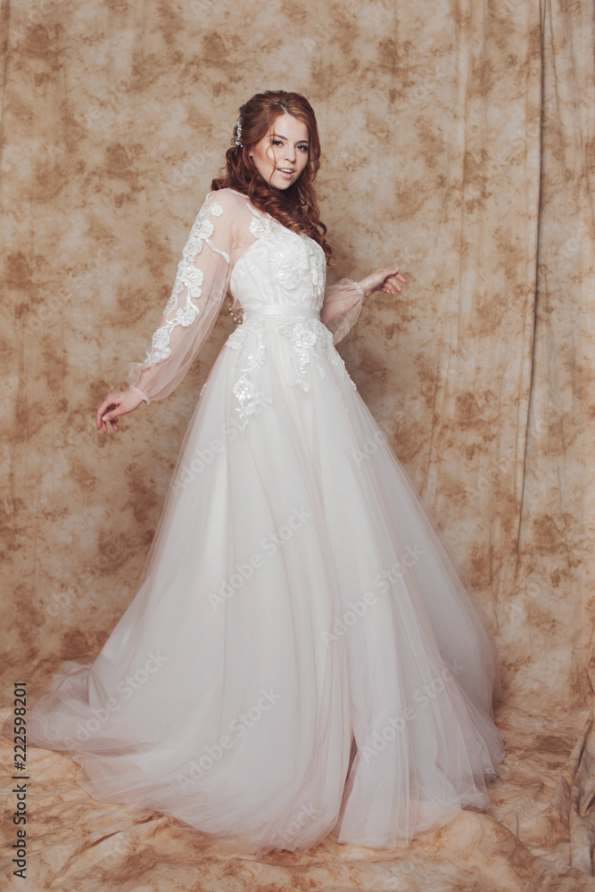 Beautiful and romantic bride in wedding dress with long sleeves. Young redheaded woman in wedding dress