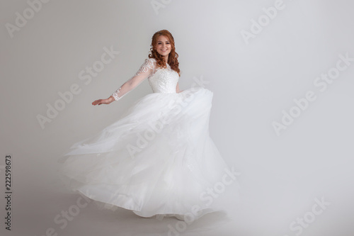 Dancing young woman in wedding dress. Charming bride on Light background.