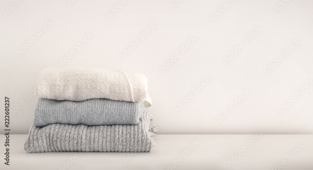 Stack of neatly folded woolen knitwear. Minimal lifestyle, capsule wardrobe. Autumn-winter wardrobe concept. Light and airy, horizontal copy space - obrazy, fototapety, plakaty 