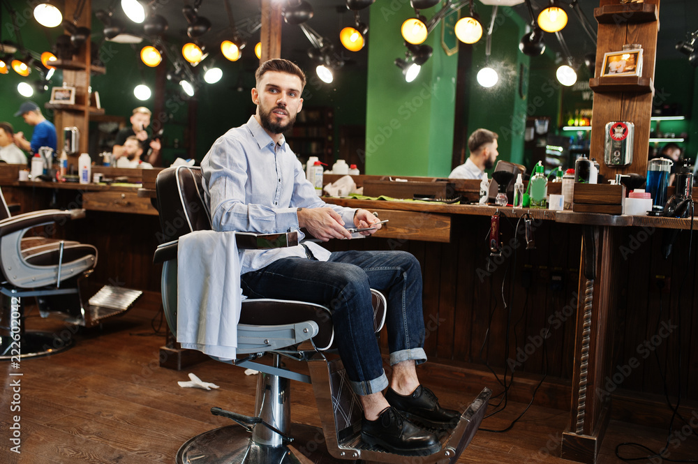 Handsome bearded man barber sitting on chair at the barbershop.